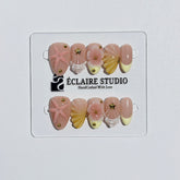 Summer Eclaire Nail Studio Luxury short almond press-on nails featuring a sheer nude base with butter yellow French tips, hand-sculpted 3D pink starfish, amber-tinted 3D seashells, and flowers with gold accents.