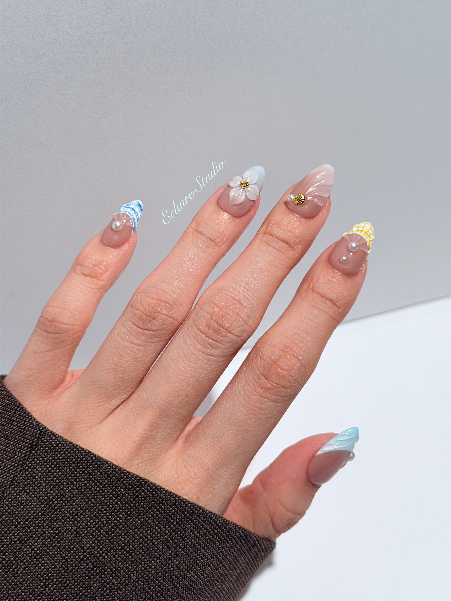 Artisanal resort-style press-on nails with a sheer nude base, pastel blue and yellow striped French tips, 3D sculpted flowers, and gold starfish charms with mini pearls.