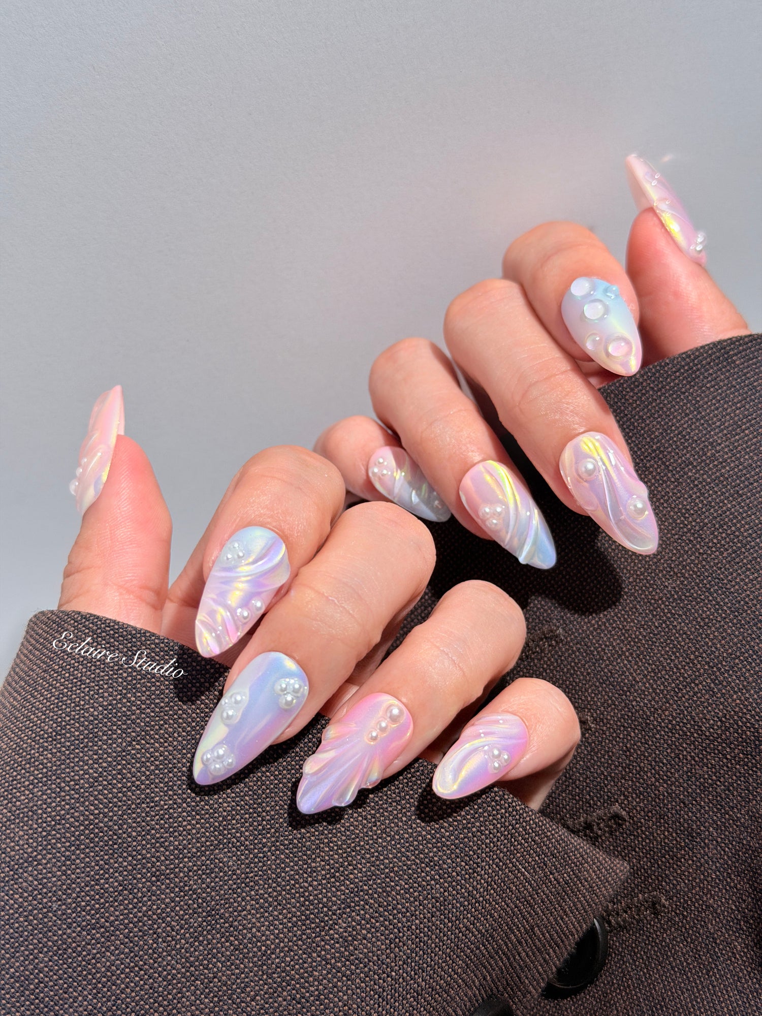 Handcrafted luxury press-on nails in a medium almond shape featuring an iridescent multi-toned glazed finish with 3D sculpted shell ridges and delicate mini pearls.