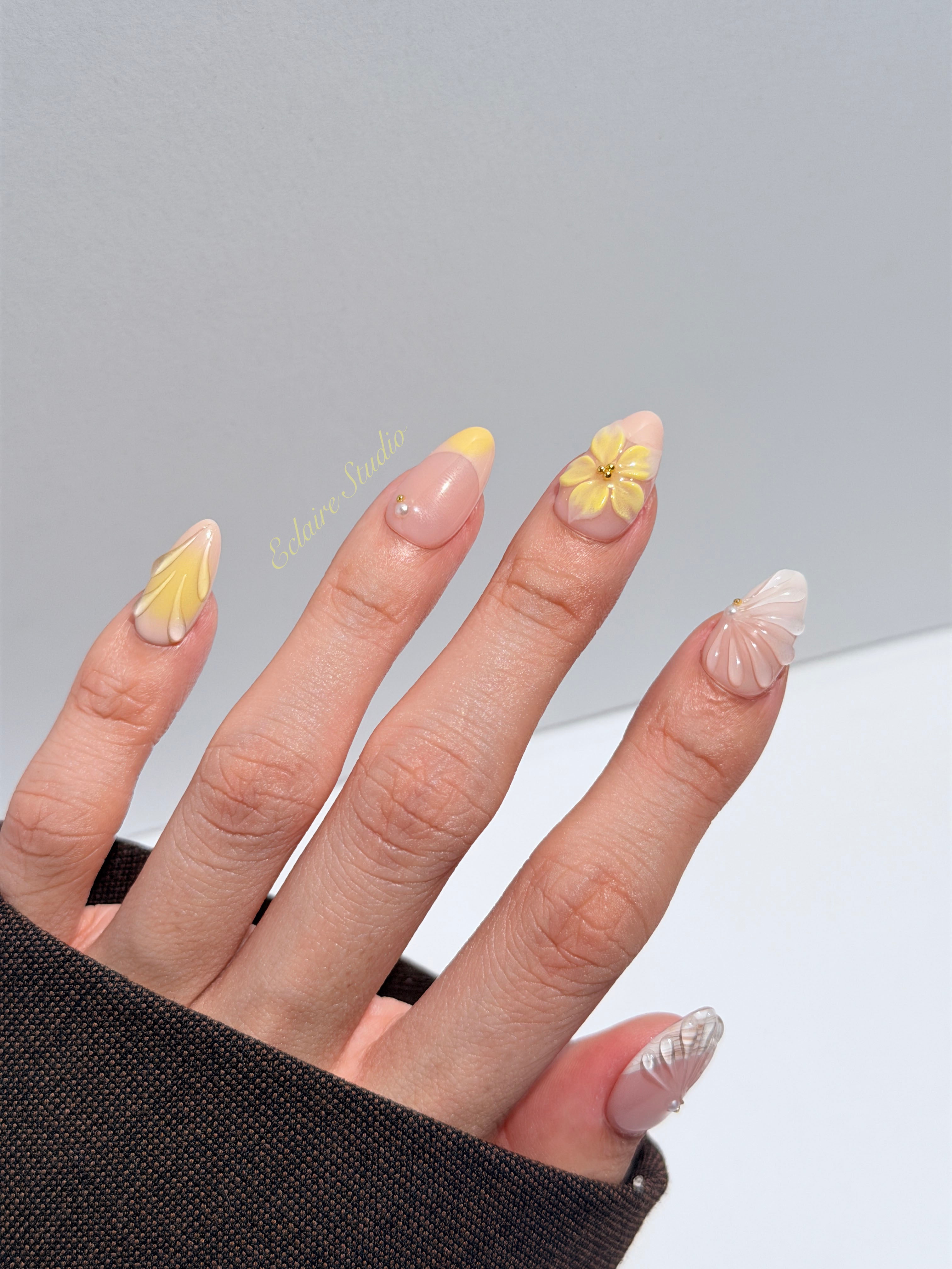 Eclaire Studio Yellow Summer short almond press-on nails featuring a sheer nude base with yellow French tips, hand-sculpted 3D flowers, frosted 3D seashells
