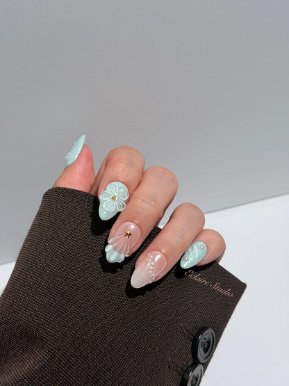 Eclaire Nail Studio 3D Summer short almond press-on nails featuring a light aqua glazed base and peachy-nude accent nails with 3D sculpted ocean waves, 3D flowers, and seashell tips with mini pearls and gold stars.