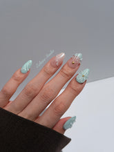 Eclaire Nail Studio 3D Summer short almond press-on nails featuring a light aqua glazed base and peachy-nude accent nails with 3D sculpted ocean waves, 3D flowers, and seashell tips with mini pearls and gold stars.