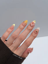 Summer Eclaire Nail Studio Luxury short almond press-on nails featuring a sheer nude base with butter yellow French tips, hand-sculpted 3D pink starfish, amber-tinted 3D seashells, and flowers with gold accents.