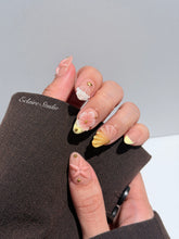 Summer Eclaire Nail Studio Luxury short almond press-on nails featuring a sheer nude base with butter yellow French tips, hand-sculpted 3D pink starfish, amber-tinted 3D seashells, and flowers with gold accents.