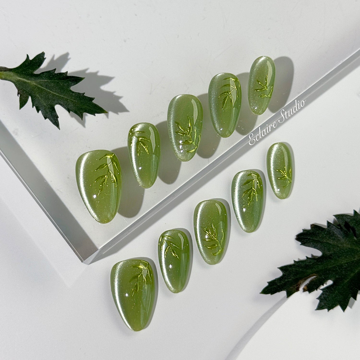 Green cat-eye press-on nails featuring layered ivy designs brushed with shiny green powder — Éclaire Nail Studio