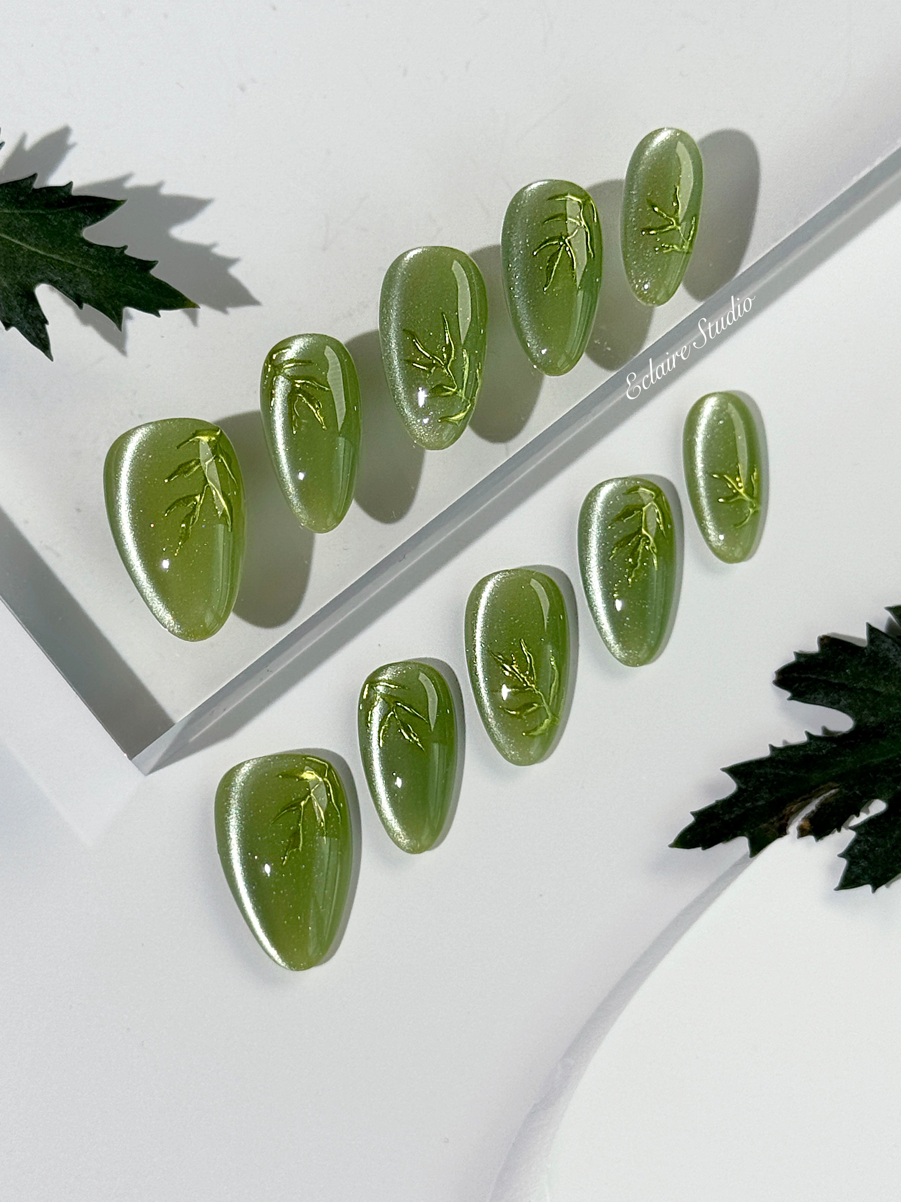 Green cat-eye press-on nails featuring layered ivy designs brushed with shiny green powder — Éclaire Nail Studio