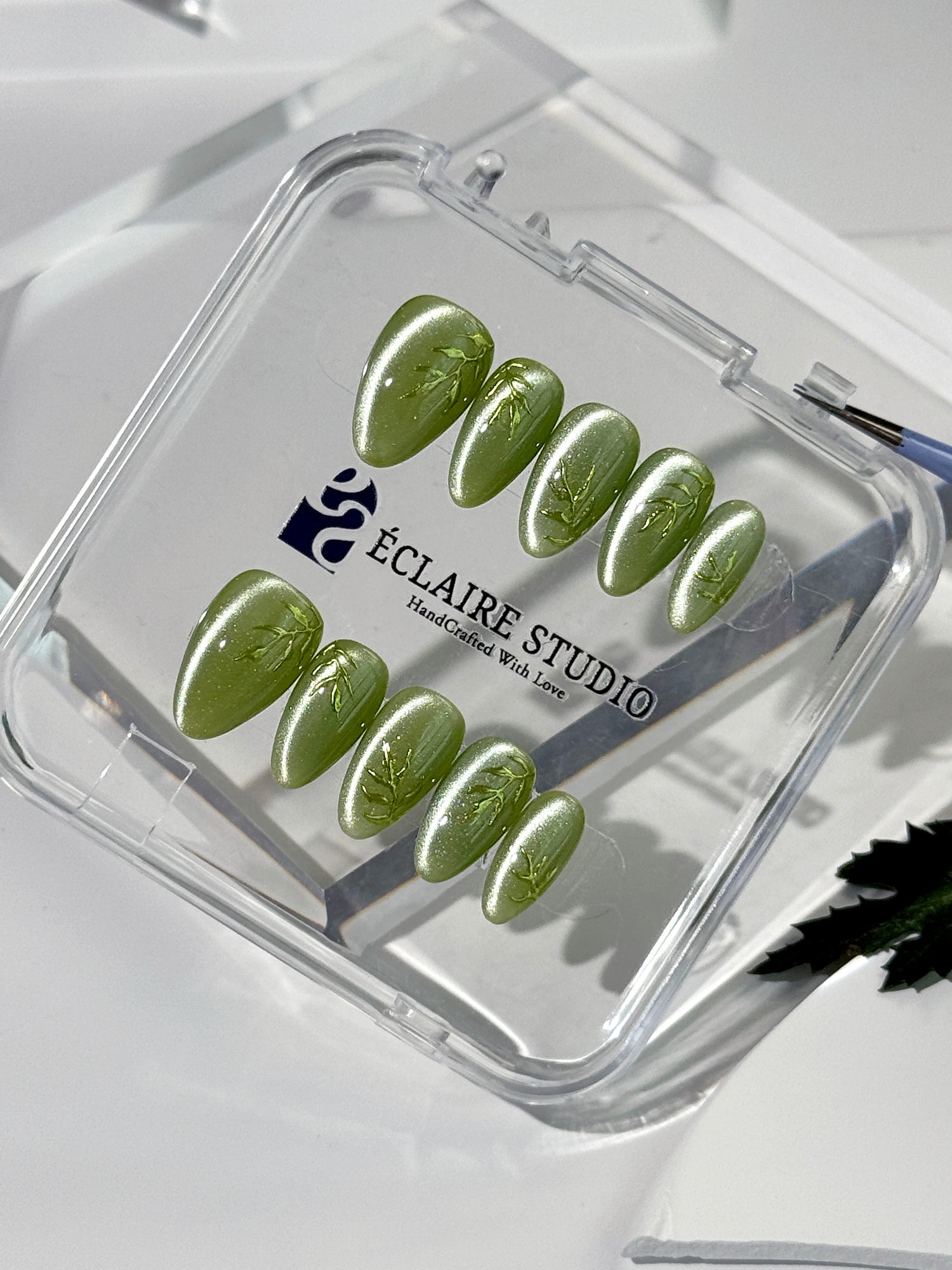Green cat-eye press-on nails featuring layered ivy designs brushed with shiny green powder — Éclaire Nail Studio