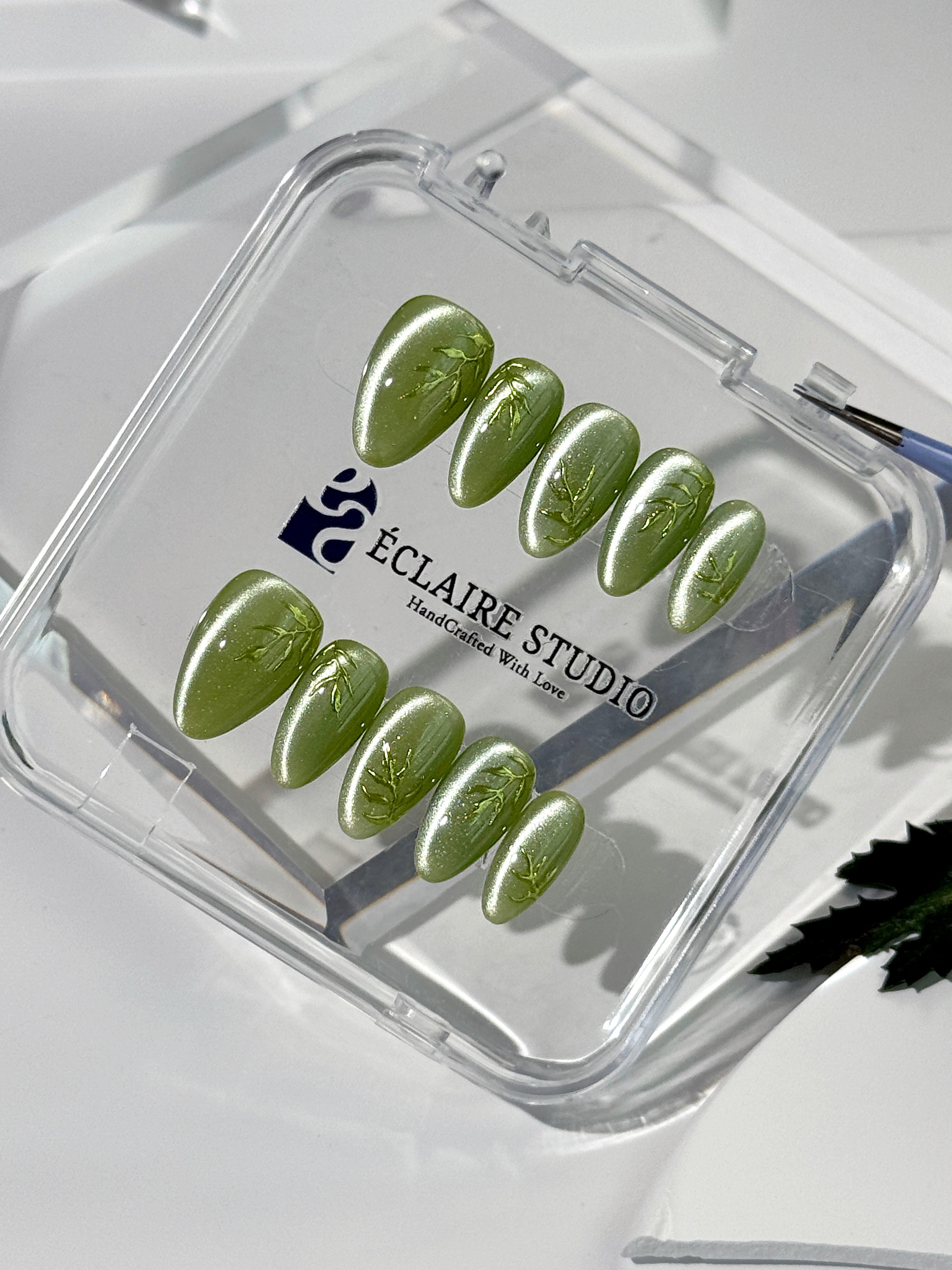 Green cat-eye press-on nails featuring layered ivy designs brushed with shiny green powder — Éclaire Nail Studio
